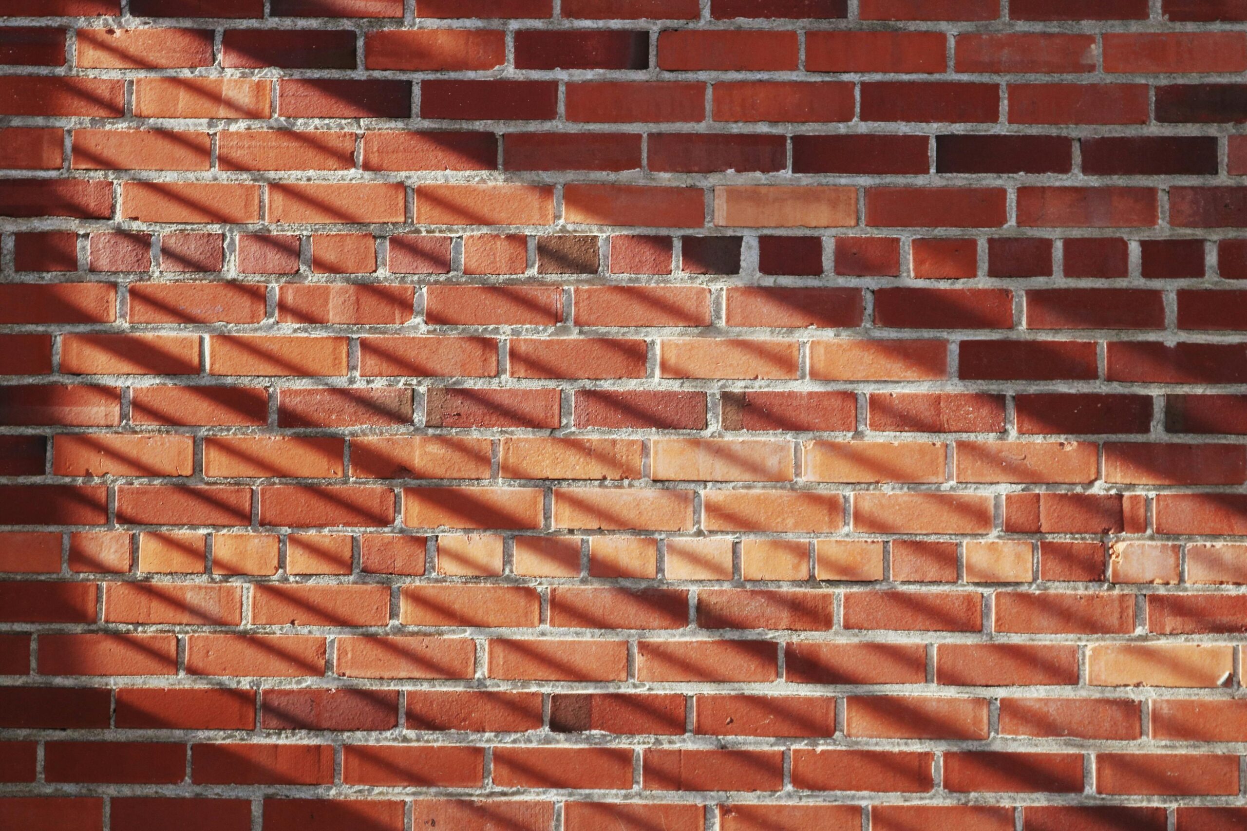 Tiiliseinän pinta ja luonnollinen valon luoma kuviointi. Tyylikäs punatiiliseinä rakennuksen julkisivussa
